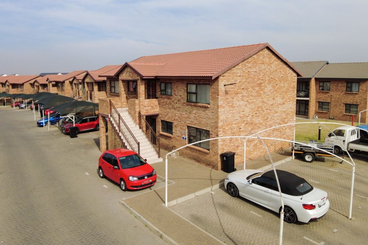 Aerial view of a multi-unit apartment complex featuring face brick construction, tiled roofing, external staircases, and dedicated paved parking with shade cloth structures.