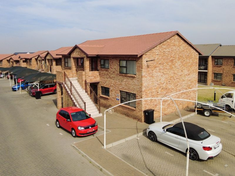 Aerial view of a multi-unit apartment complex featuring face brick construction, tiled roofing, external staircases, and dedicated paved parking with shade cloth structures.