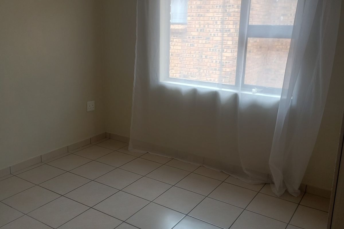 A clean, empty bedroom featuring neutral tiled flooring and a window, providing a blank canvas for personalization.