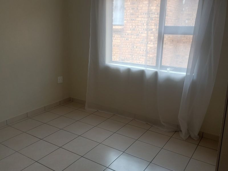 A clean, empty bedroom featuring neutral tiled flooring and a window, providing a blank canvas for personalization.