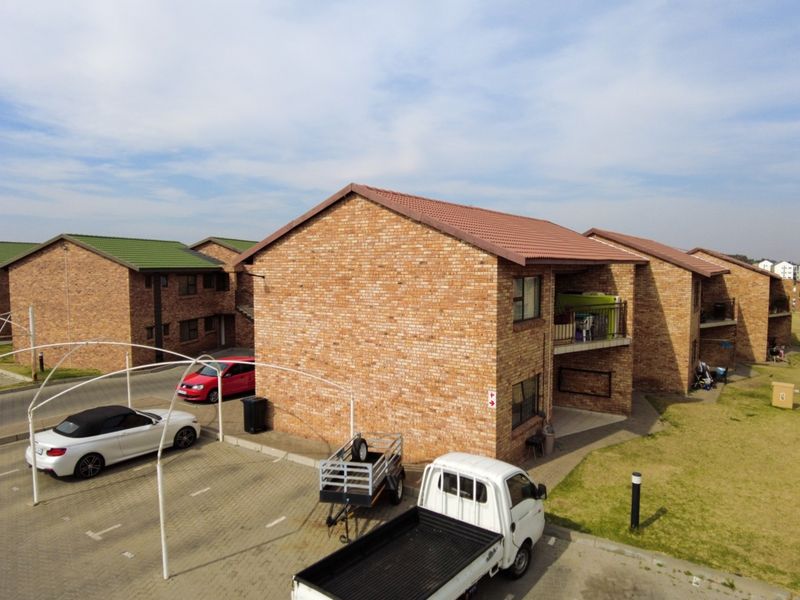 Aerial view of a face brick apartment complex featuring tiled roofs, paved parking areas, and private balconies.