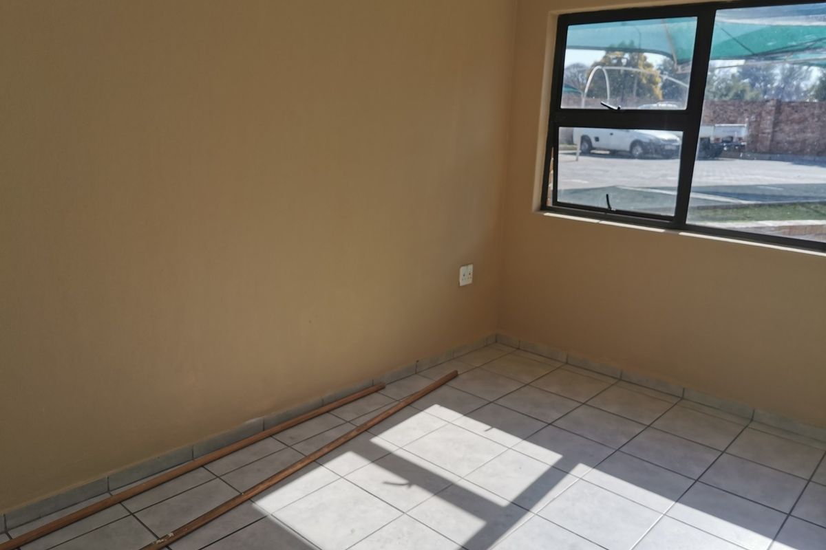 A vacant bedroom featuring neutral wall paint, tiled flooring, and a large aluminium-framed window providing natural light.