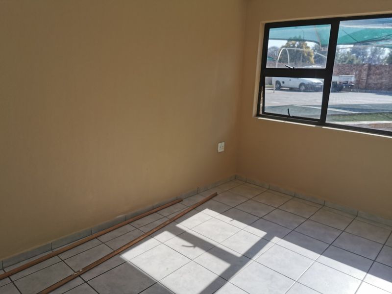 A vacant bedroom featuring neutral wall paint, tiled flooring, and a large aluminium-framed window providing natural light.