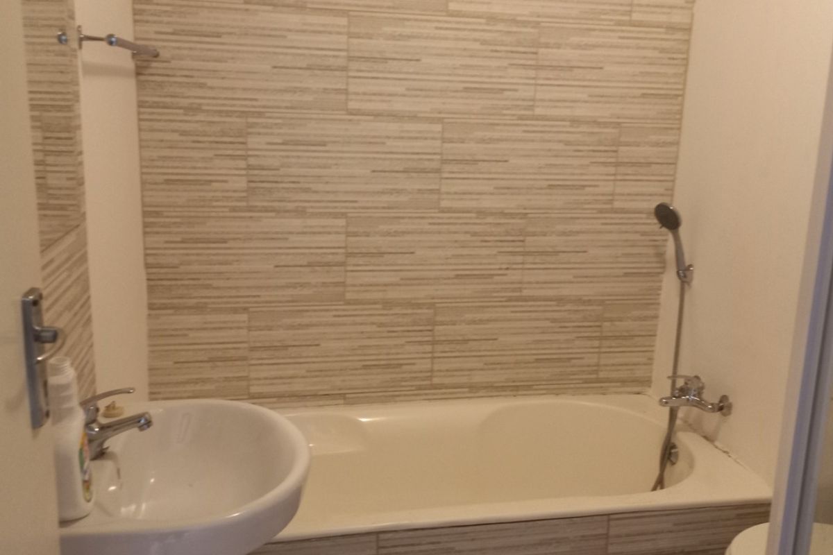A functional bathroom featuring a pedestal sink, a bathtub with a shower mixer, and neutral textured wall tiling.