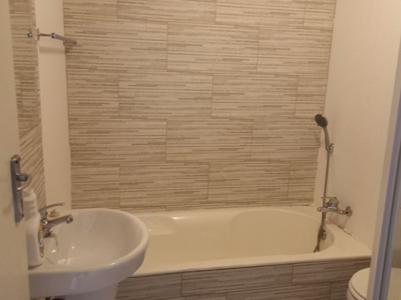 A functional bathroom featuring a pedestal sink, a bathtub with a shower mixer, and neutral textured wall tiling.