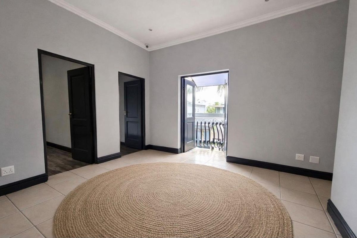 A bright, empty bedroom featuring neutral grey walls, tiled flooring, dark contrasting door frames, and direct access to a private balcony.