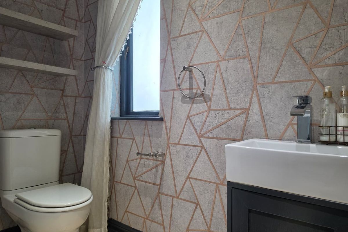 A modern bathroom featuring a vanity with a basin, a toilet, and geometric patterned wallpaper with floating shelving.