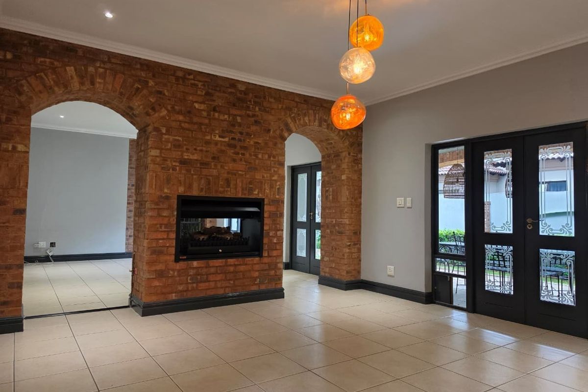Spacious living area featuring striking exposed brick archways, a built-in fireplace, tiled flooring, and direct access to the outdoor area through glass panelled doors.