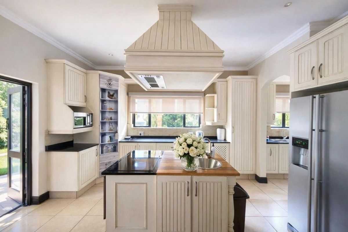 A well-appointed kitchen featuring a central island with a cooktop and sink, ample cabinetry, and integrated appliances, opening to an outdoor area.