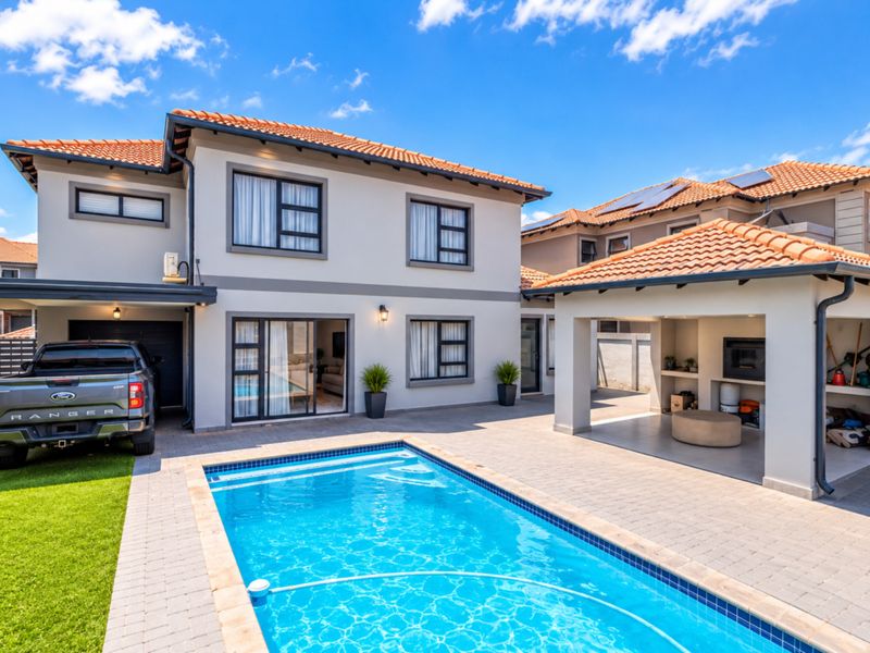 Rear exterior view featuring a swimming pool, paved patio area, and a covered entertainment space with a built-in braai.