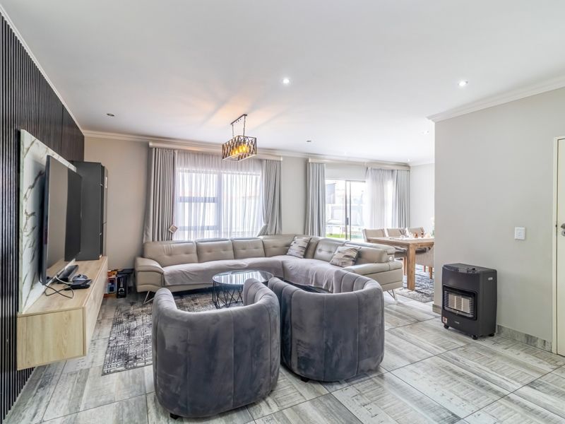 Spacious open-plan living and dining area featuring modern tiled flooring, recessed lighting, and a contemporary media wall with slatted timber accents.