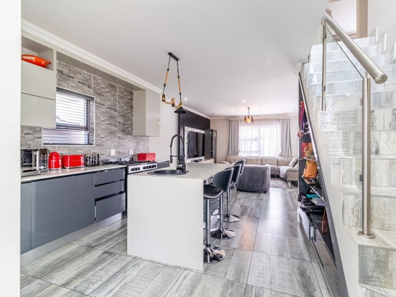 Modern open-plan living area featuring a sleek kitchen with stone island, tiled flooring, and a contemporary staircase with glass balustrade.