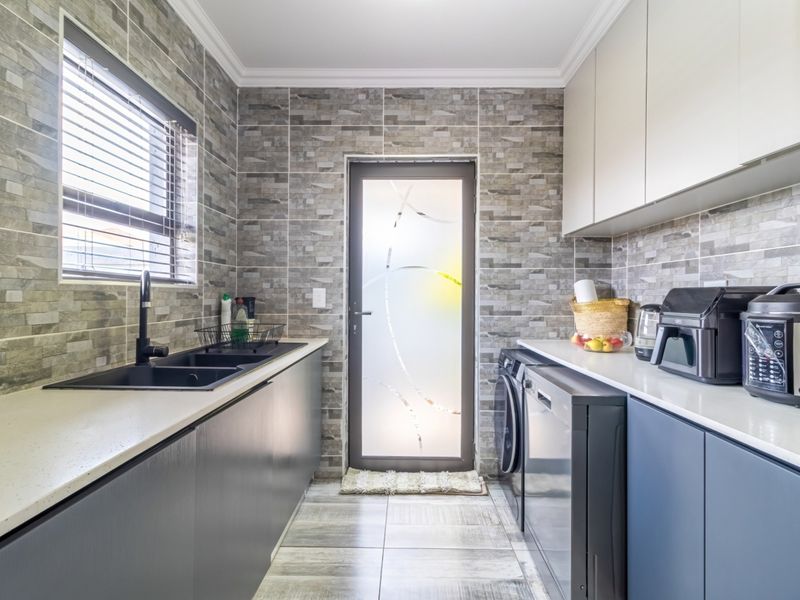 Modern scullery featuring stone-look wall tiles, sleek matte black fixtures, ample built-in cabinetry, and dedicated plumbing connections for laundry appliances.