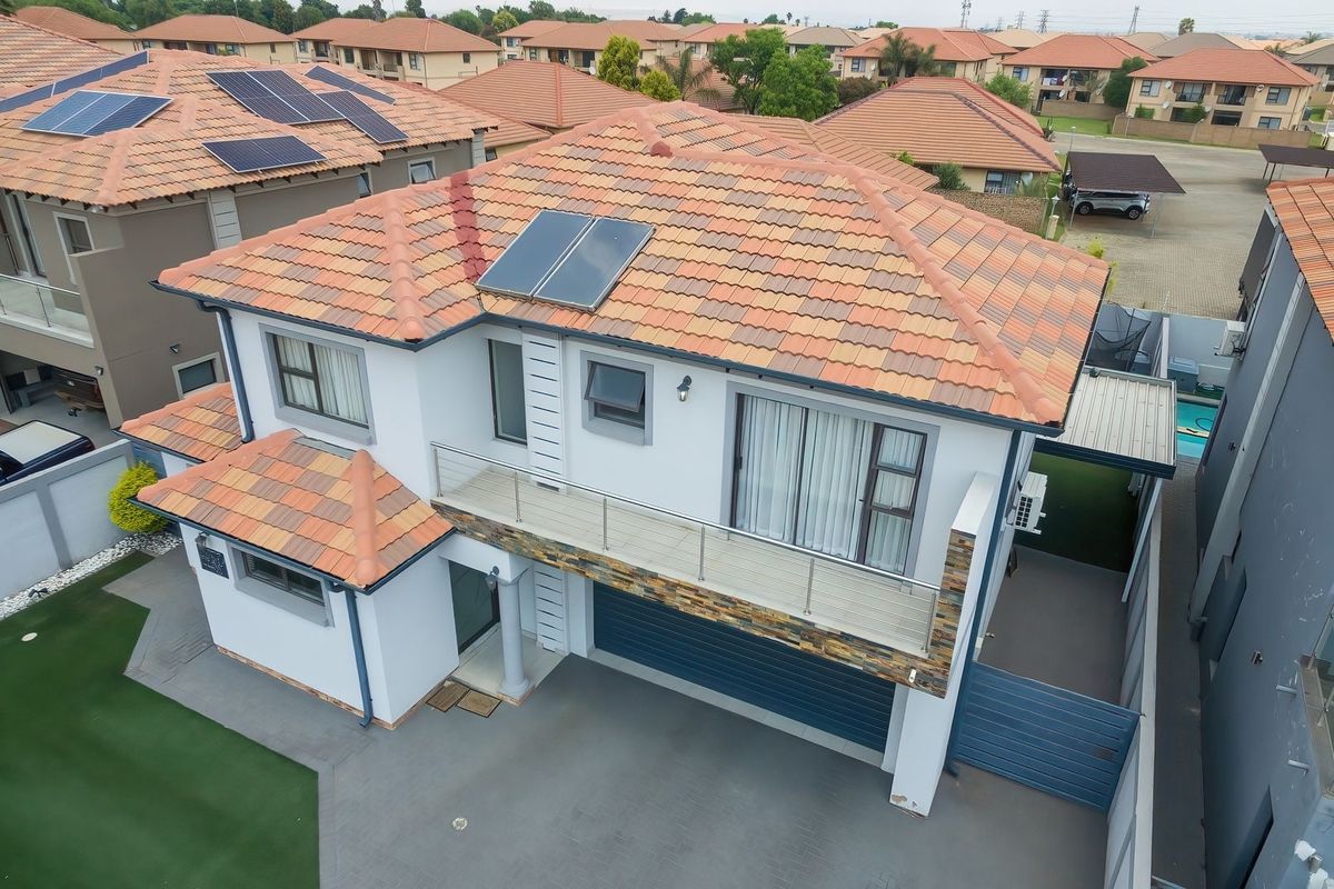 Aerial view of a modern cluster home featuring a tiled roof with solar panels, a balcony with glass balustrades, stone cladding, and a paved driveway.