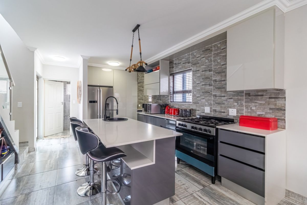 Modern kitchen featuring a central island with stone countertops, gas stove, built-in oven, stone tile backsplash, and sleek cabinetry.