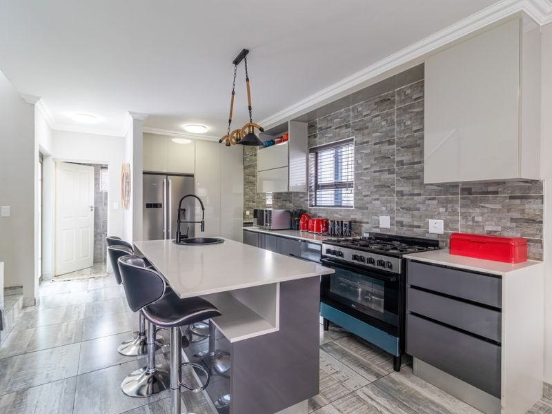 Modern kitchen featuring a central island with stone countertops, gas stove, built-in oven, stone tile backsplash, and sleek cabinetry.