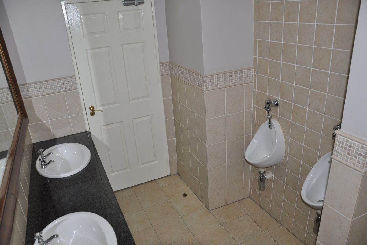 A clean, functional office restroom featuring dual vanity basins with granite countertops and wall-mounted urinals with neutral tiled finishes.