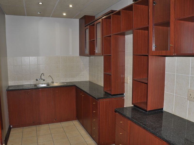 A functional kitchen area featuring dark wood-look cabinetry, granite countertops, a stainless steel sink, and neutral tiled backsplash and flooring.
