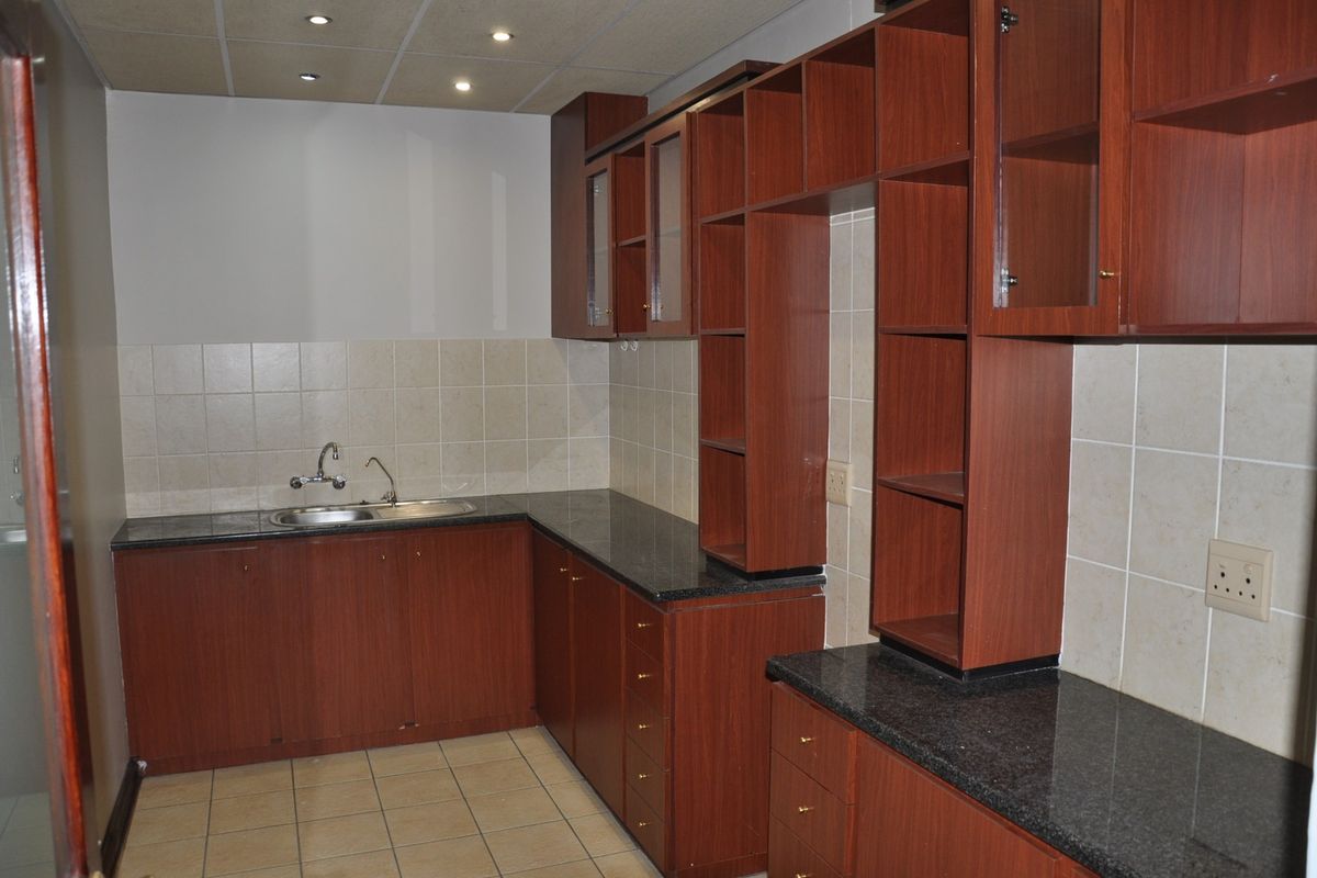 A functional kitchen area featuring dark wood-look cabinetry, granite countertops, a stainless steel sink, and neutral tiled backsplash and flooring.