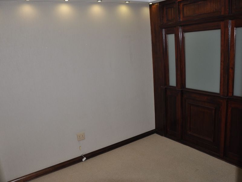 A clean, empty office space featuring warm timber paneling, a frosted glass door, and recessed ceiling lighting, providing a professional and versatile work environment.