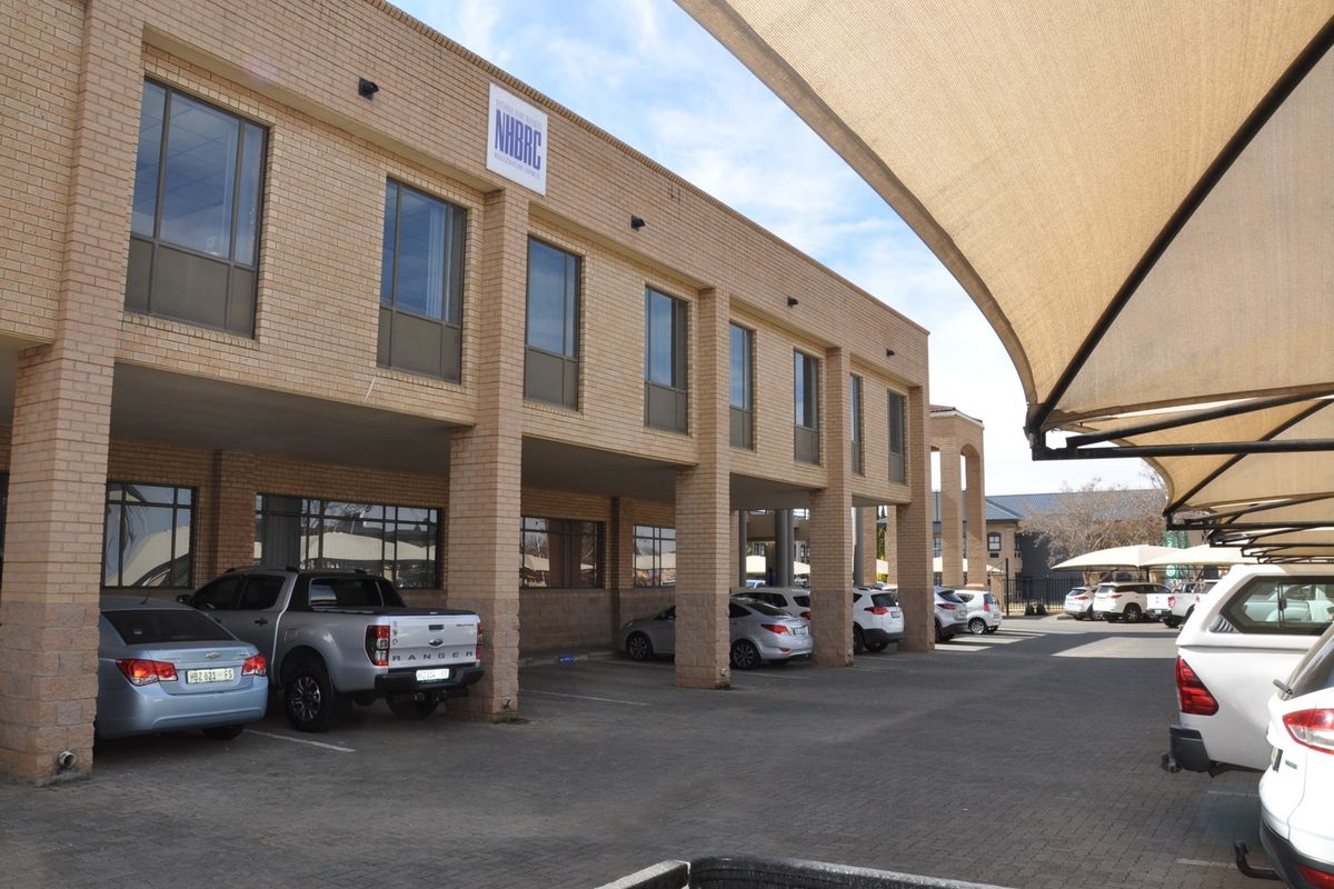 Exterior view of a multi-story brick office building featuring a covered parking area with shade sails and paved driveway access.