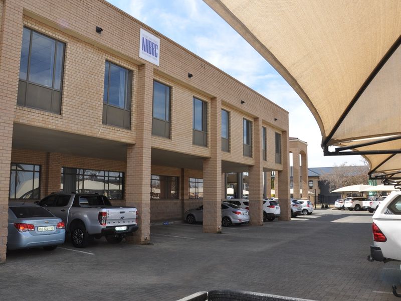 Exterior view of a multi-story brick office building featuring a covered parking area with shade sails and paved driveway access.