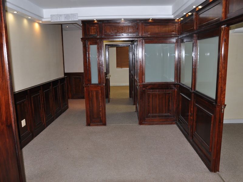 Professional office space featuring classic dark wood paneling, integrated frosted glass partitions, recessed ceiling lighting, and neutral carpeting.