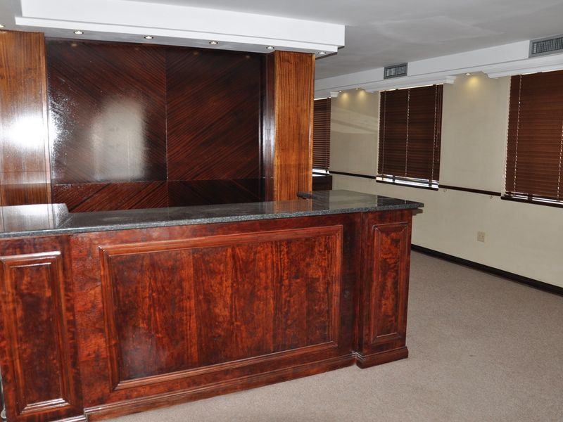 A professional office bar area featuring a high-quality built-in wooden counter with granite top, recessed lighting, and venetian blinds.