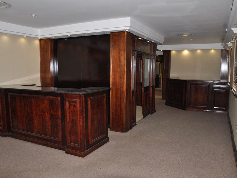 Spacious office area featuring built-in dark wood reception counters, recessed ceiling lighting, and neutral carpeting throughout the professional workspace.