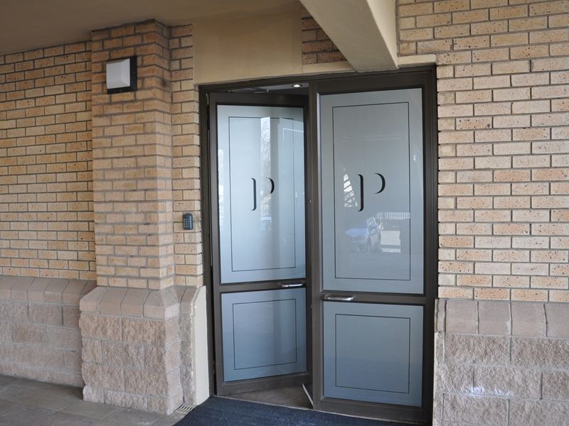 A professional office entrance featuring a brick facade, secure double glass doors with frosted detailing, and integrated keypad access control.