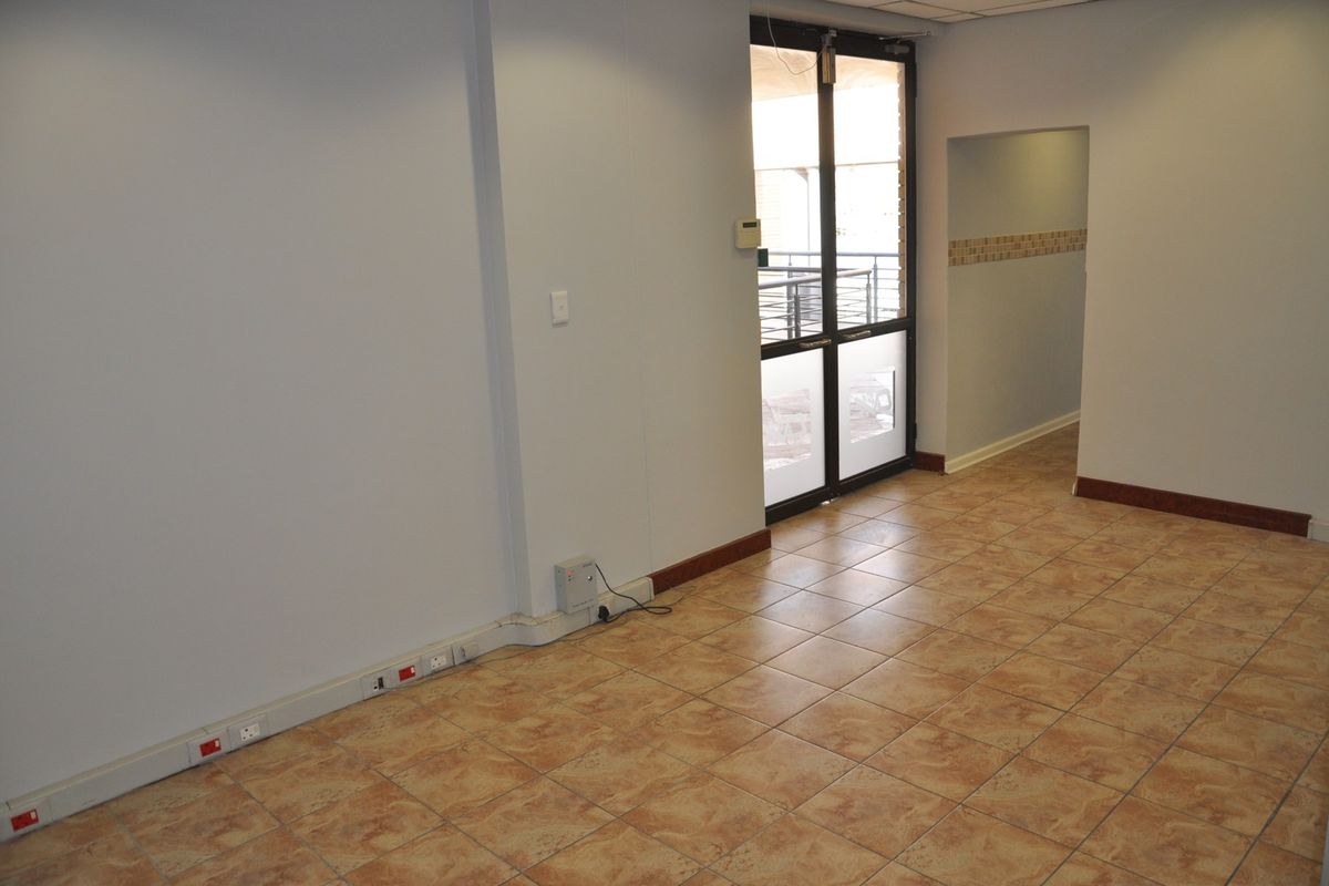 An empty office space featuring tiled flooring, electrical trunking along the baseboards, and a glass panel door leading to an exterior area.