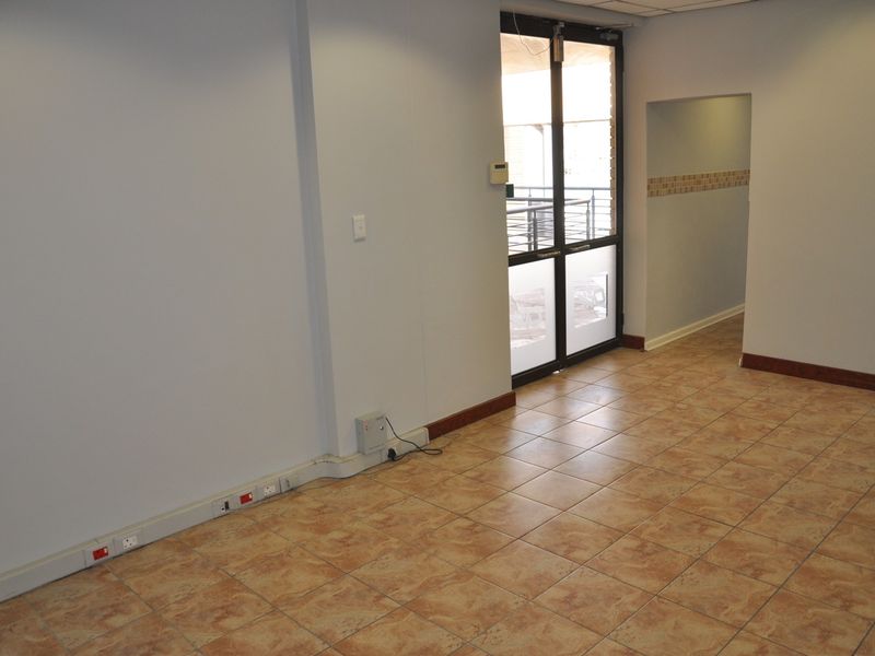 An empty office space featuring tiled flooring, electrical trunking along the baseboards, and a glass panel door leading to an exterior area.