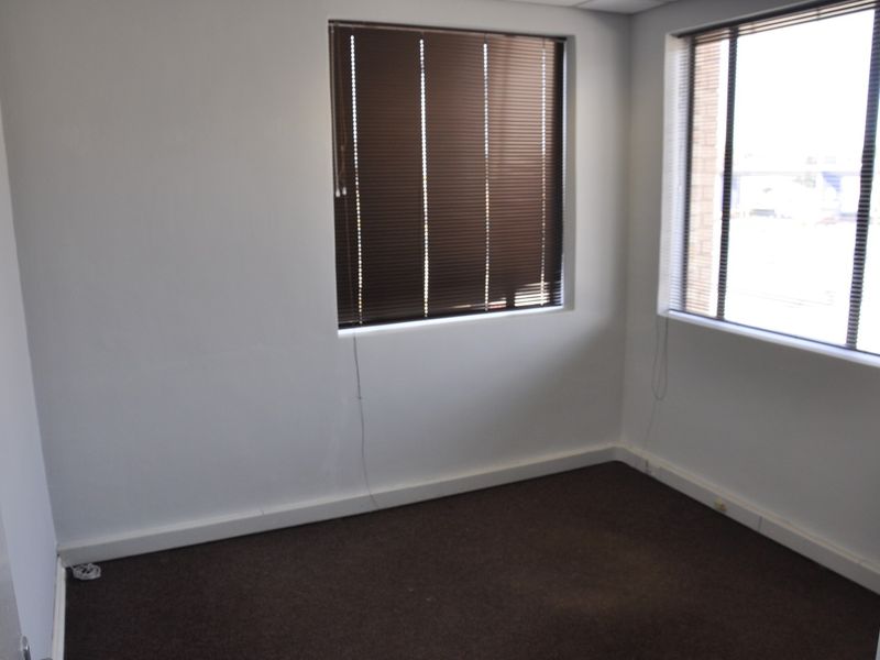 A vacant office space featuring neutral walls, dark carpeting, and fitted venetian blinds, providing a clean and functional environment for professional use.