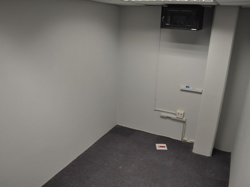 A clean, empty office space featuring grey carpet flooring, a wall-mounted network cabinet, and neutral painted walls.