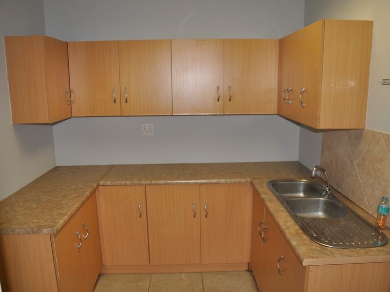 A functional office kitchenette featuring light wood-look cabinetry, laminate countertops, and a double stainless steel sink with tiled splashback.