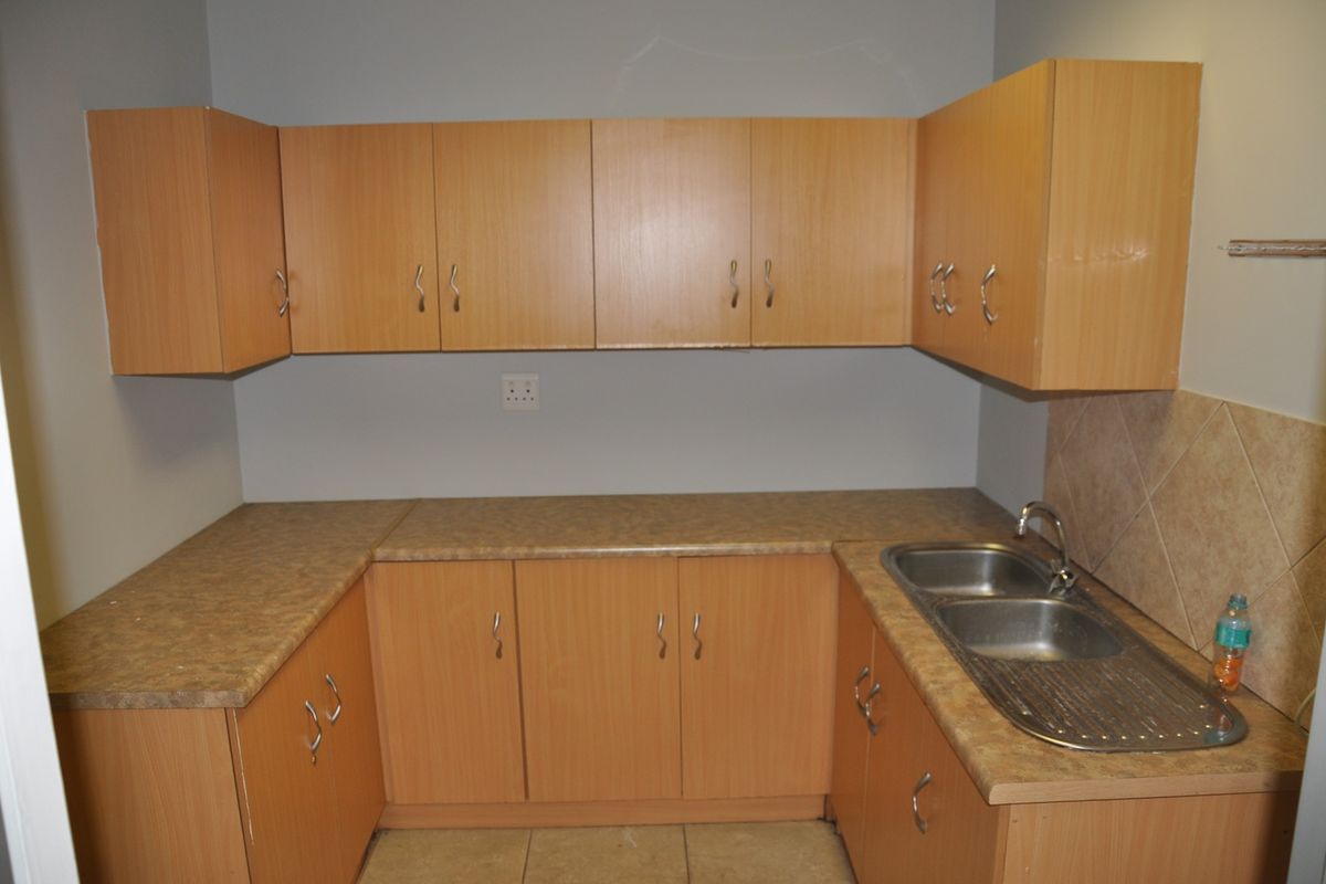 A functional office kitchenette featuring light wood-look cabinetry, laminate countertops, and a double stainless steel sink with tiled splashback.