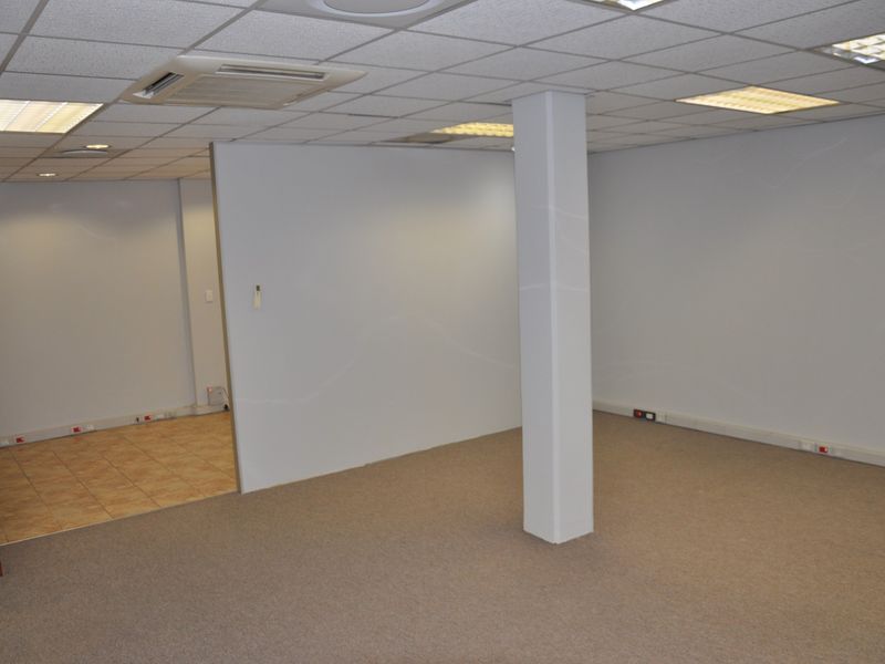An open-plan office space featuring a suspended ceiling with recessed lighting, ducted air conditioning, carpeted and tiled flooring, and a central structural column.