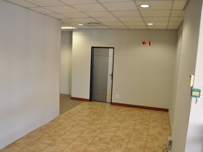 A vacant office space featuring tiled flooring, a suspended ceiling with recessed lighting, and a neutral wall finish.