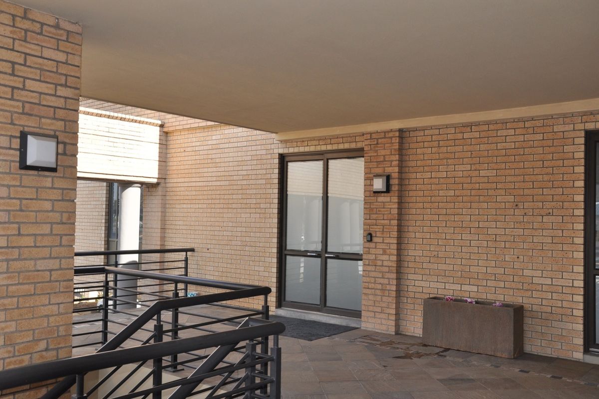 A clean and well-maintained office building entrance featuring brick exterior walls, glass double doors, and modern metal railings.