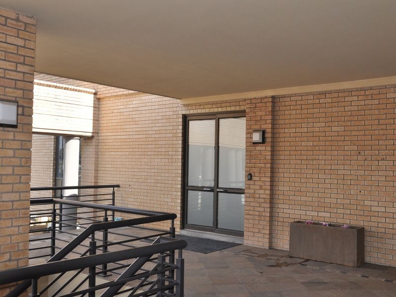 A clean and well-maintained office building entrance featuring brick exterior walls, glass double doors, and modern metal railings.