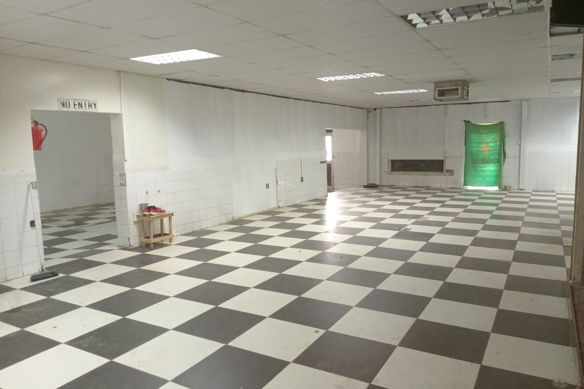 Spacious open-plan retail area featuring a checkered tiled floor, suspended ceiling with recessed lighting, and partial wall tiling throughout the interior space.