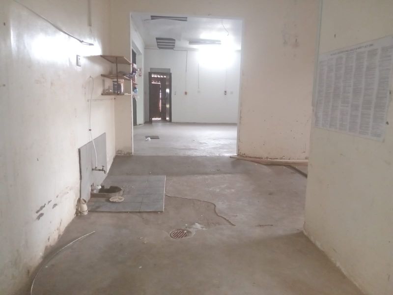 An empty utility or service area featuring concrete flooring, a wall-mounted tap, and a floor drain, requiring maintenance and cosmetic updates.