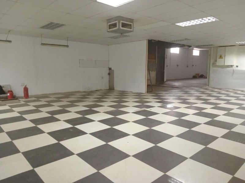 Spacious open-plan retail area featuring checkered tile flooring, suspended ceiling with recessed lighting, and an integrated electrical distribution board.