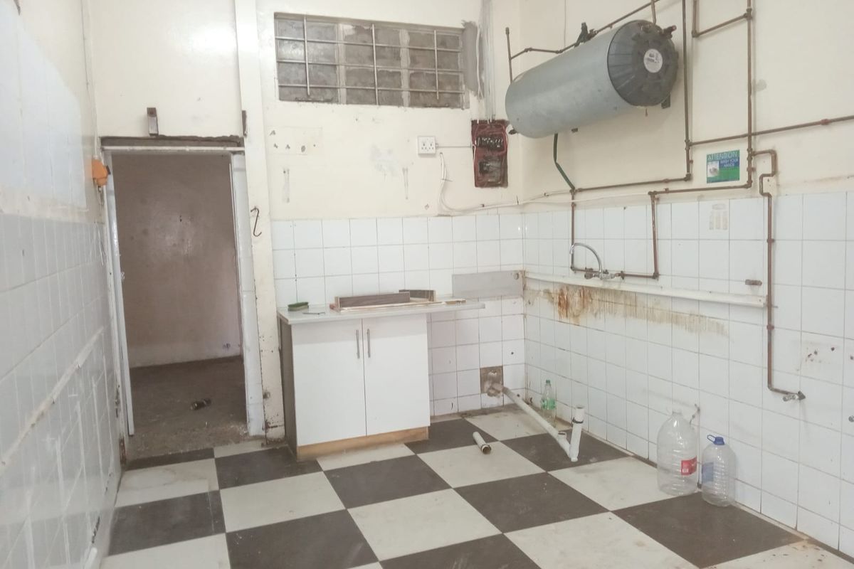 A vacant utility or kitchen area featuring checkerboard floor tiles, wall-mounted water heater, and exposed plumbing, requiring significant renovation and cosmetic updates.