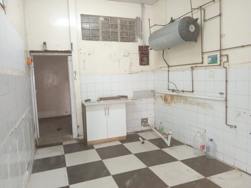 A vacant utility or kitchen area featuring checkerboard floor tiles, wall-mounted water heater, and exposed plumbing, requiring significant renovation and cosmetic updates.