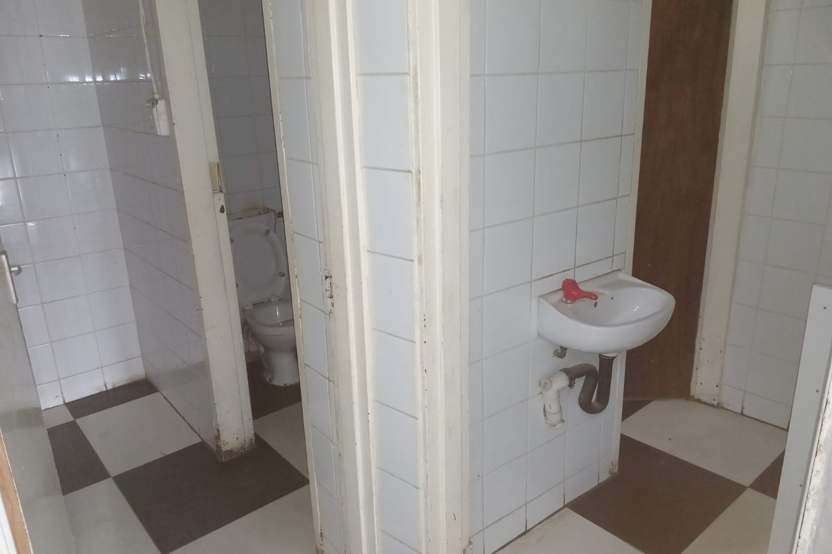 A functional bathroom area featuring a wall-mounted basin, toilet, and tiled finishes, currently in need of cosmetic updates and maintenance.
