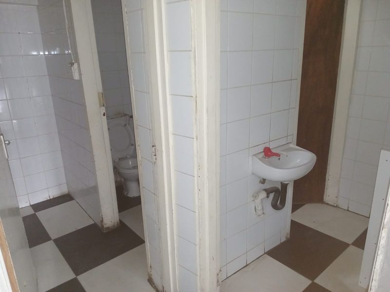 A functional bathroom area featuring a wall-mounted basin, toilet, and tiled finishes, currently in need of cosmetic updates and maintenance.