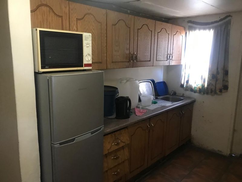 A compact kitchen featuring dated wooden cabinetry, a stainless steel sink, and tiled flooring, requiring cosmetic updates to improve its overall appeal.