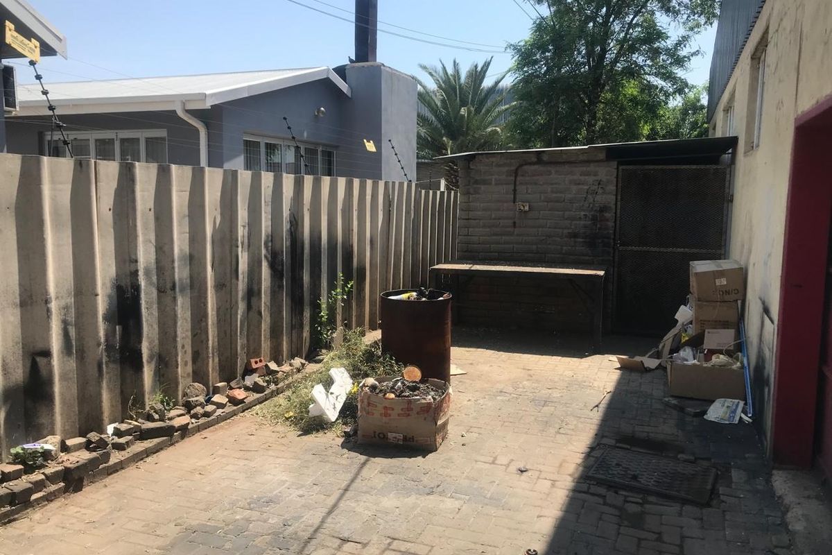 A rear courtyard area featuring paved flooring, a precast boundary wall, and a small brick storage structure.