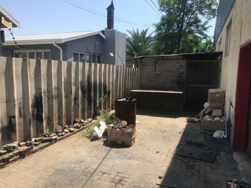 A rear courtyard area featuring paved flooring, a precast boundary wall, and a small brick storage structure.